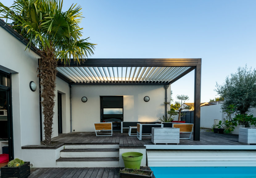 Trendy outdoor patio pergola. garden lounge, chairs, metal grill surrounded by landscaping